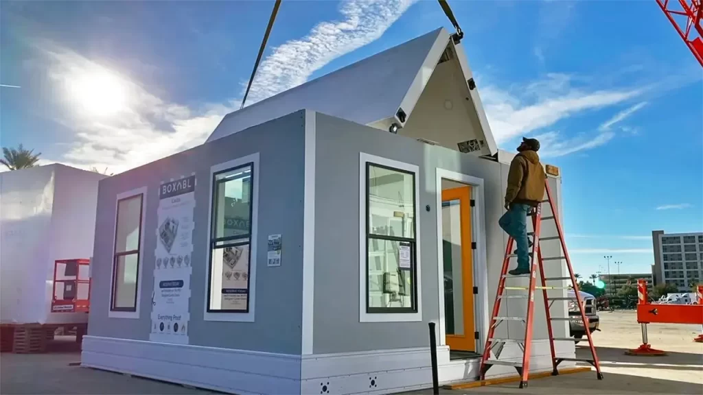 A builder standing on a ladder watching as the roof is begin lowered on a small house at the International Builders' Show